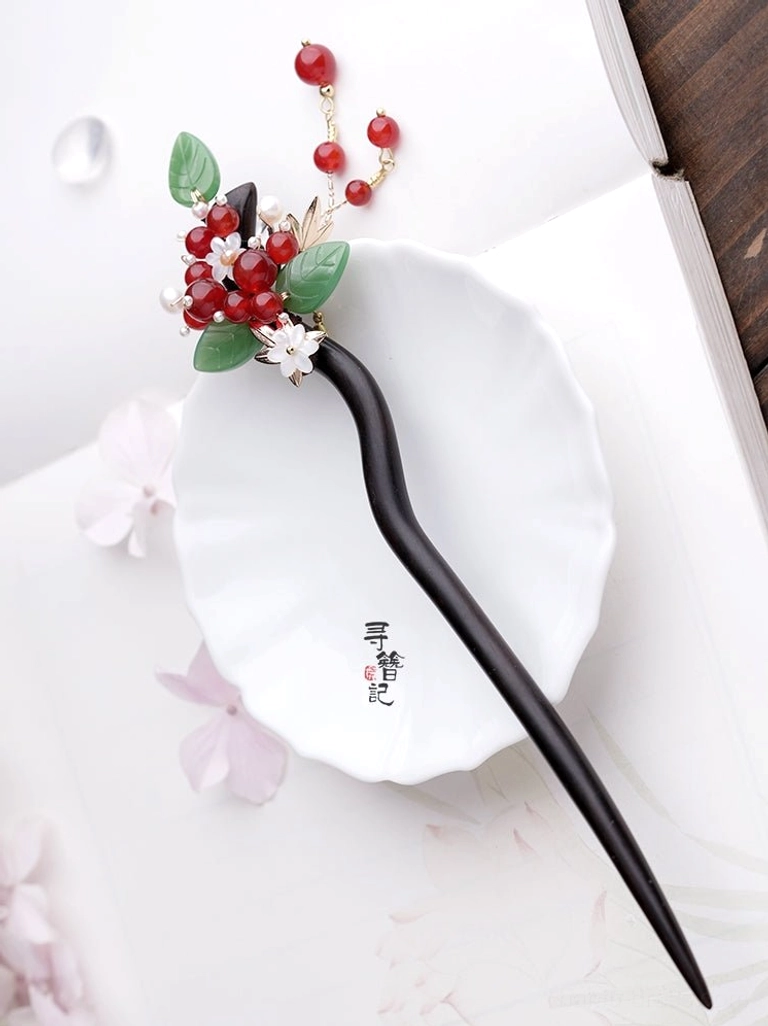 Decorative red bean Hanfu hairpin displayed on a white ceramic plate with red beads, green leaves, white flower, and tassel branch