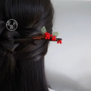 Handmade red berry Chinese hair stick worn in long dark Hanfu-style hair with wooden branch design, red glass berries, green leaf beads, and brown thread wrapping