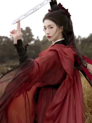 Side back view of a red and black warrior Hanfu with wide draped sleeves, sheer layered fabric, gradient dark red hem, black wrist wraps, and floral hair ornaments