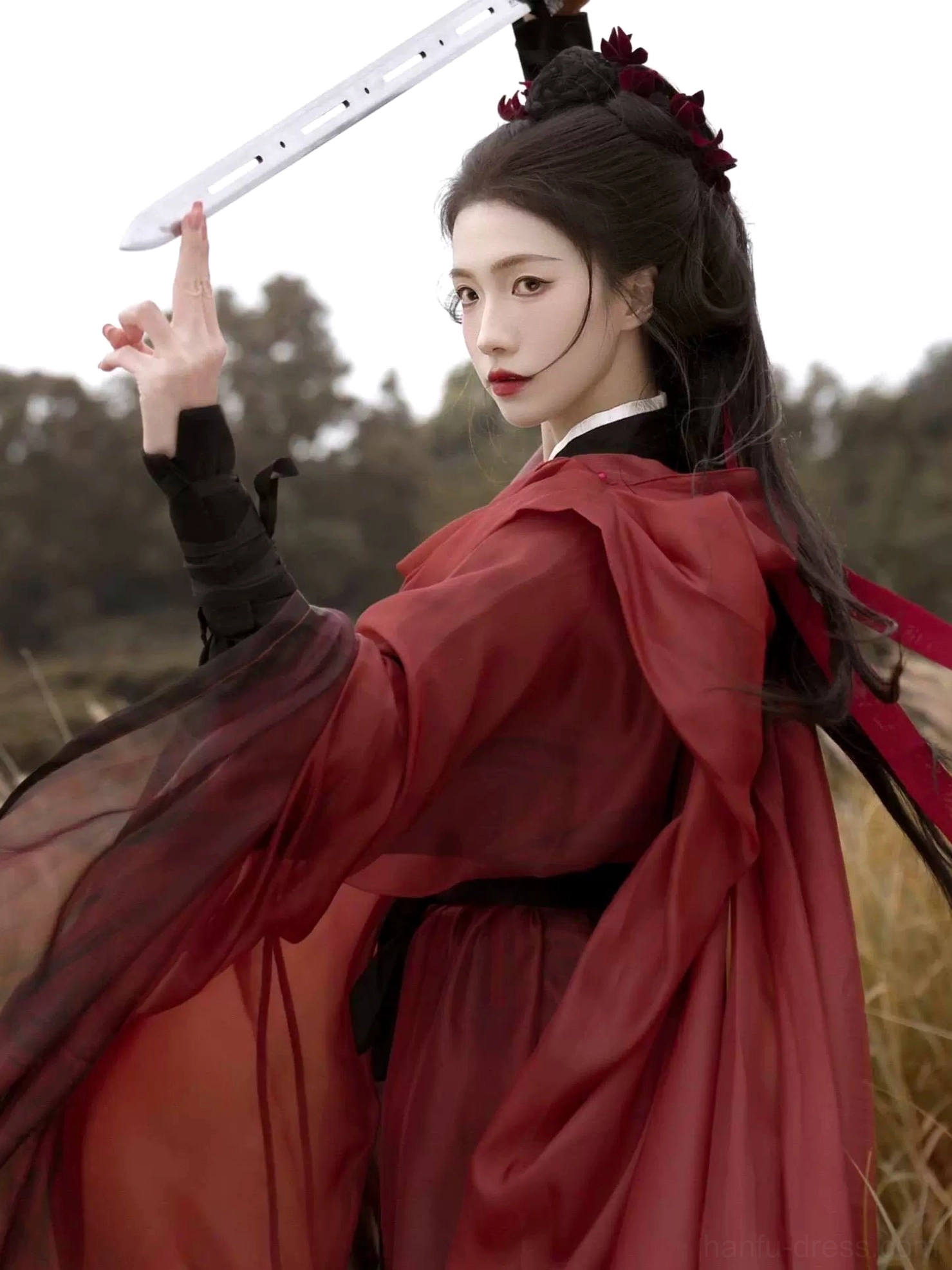 Side back view of a red and black warrior Hanfu with wide draped sleeves, sheer layered fabric, gradient dark red hem, black wrist wraps, and floral hair ornaments