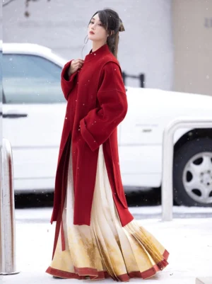 Red burgundy Hanfu-style wool coat with Chinese stand collar and frog closure styled with a gradient gold mamian skirt in snow