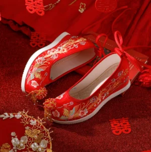Side three-quarter view of red Chinese wedding shoes for women featuring golden phoenix floral embroidery, red tassels, rear ribbon ties, and concealed wedge heels