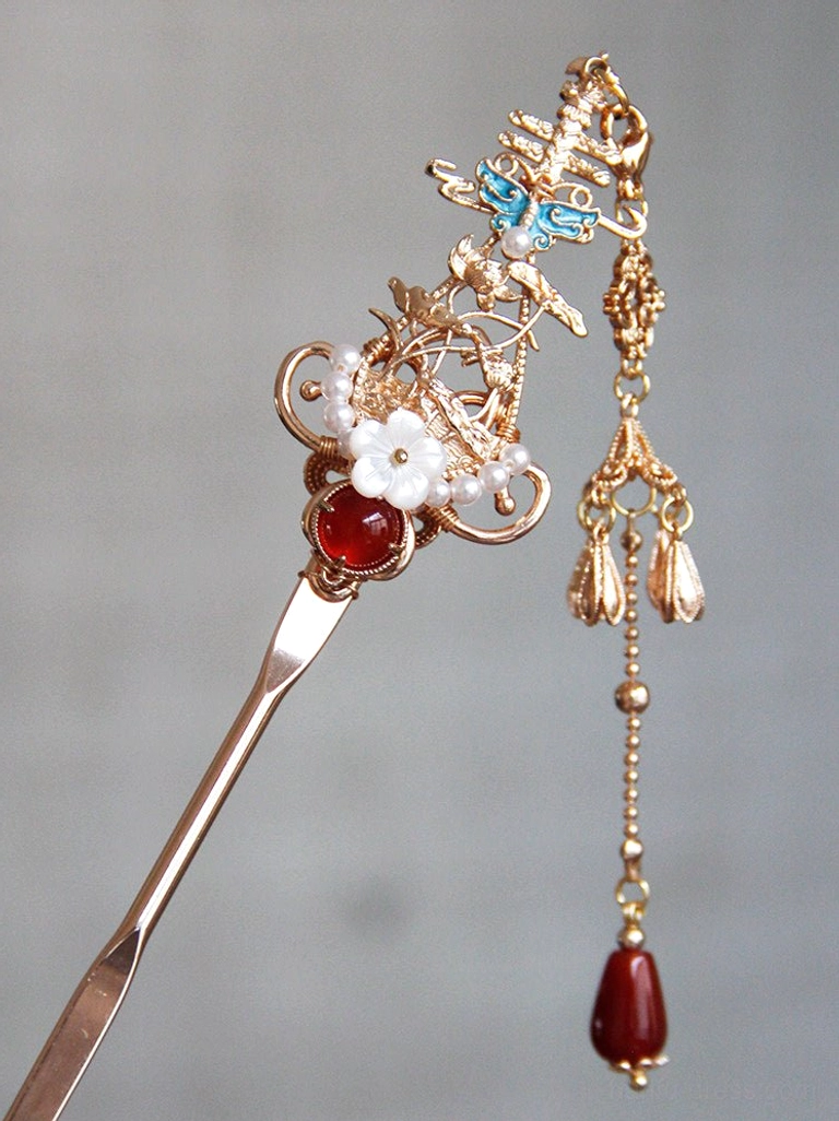 Close-up of a red Chinese hair stick with red agate bead, white flower decoration, blue enamel butterfly and long red tassel with metal fringe