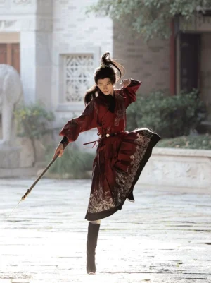 Full-body side-front view of a man wearing a red chivalrous swordsman Hanfu robe with black boots, waist belt, silver hem trim, and a traditional sword