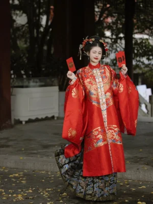 Full-length front view of a red embroidered Ming Dynasty bridal Hanfu with standing collar, wide sleeves, and dark patterned Mamian skirt