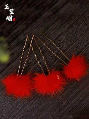 Top view of red furball Chinese Hanfu hair pins with golden U-shaped hair sticks on a dark wood background