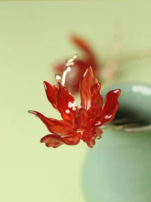 Close-up of a red glazed floral Hanfu hair pin with translucent burgundy petals, gold-tone branch ornaments, white faux pearl stamens, and a U-shaped hair stick