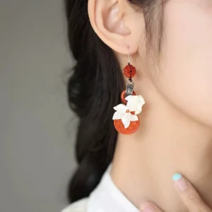 Red jade koi tassel Chinese earrings shown worn on the left ear, featuring carved white shell koi, hollow red pendants, red beads, and vintage silver-tone details