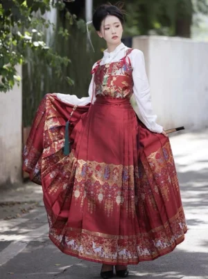 Red Ming-style hanfu mamianqun horse face skirt with ornate gold embroidered hem and patterned bustier shown in an outdoor garden setting