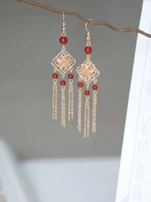 Red onyx tassel Chinese earrings displayed on a wooden twig with an antique gold rhombic floral frame, red beads, and cascading metal chains