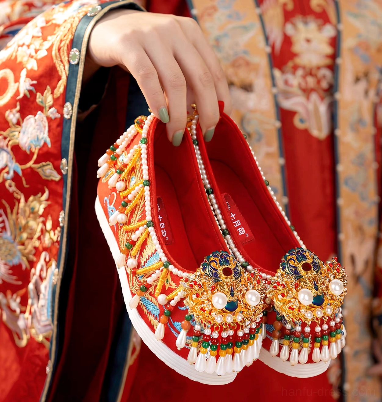 Pair of red traditional Chinese bridal Hanfu shoes with elaborate gold embroidery, jeweled toe ornaments, tassels, and thick white platform soles