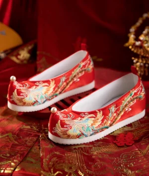 Pair of red embroidered Chinese bridal shoes for Hanfu wedding outfit featuring phoenix motifs, pearl toe details, and white soles