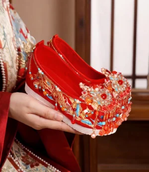 Side view of red phoenix embroidered Chinese bridal Hanfu shoes with beaded pearl tassels, red lining, and white platform rubber sole for Xiuhefu wedding attire