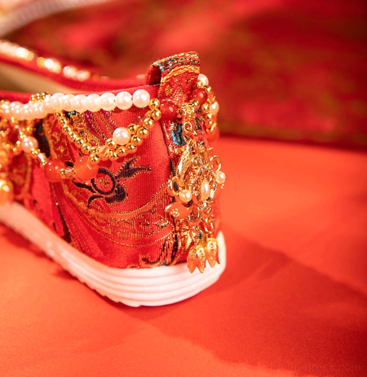 Rear side view of red embroidered Chinese bridal Hanfu shoes with pearl chain decoration and layered white platform sole