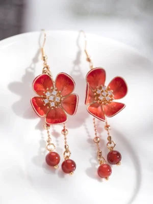 Red plum blossom velvet flower Chinese dangle earrings displayed on a white porcelain plate with gold chains rhinestone centers and red bead tassels