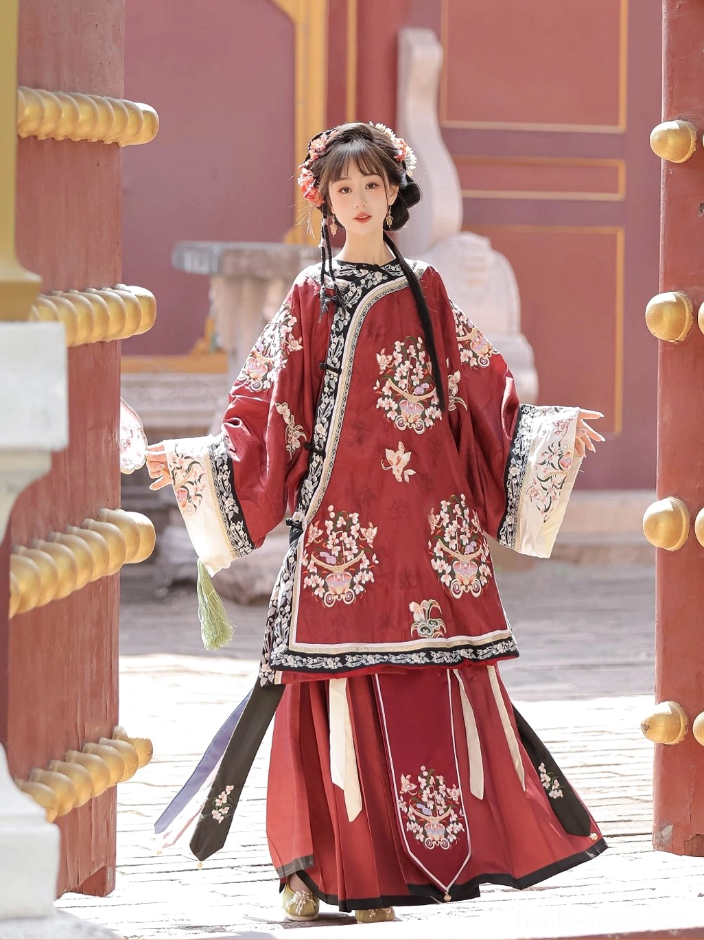 Front three-quarter view of a deep red Qing Dynasty Han women's blouse with wide sleeves and coordinated floral embroidery in a palace setting