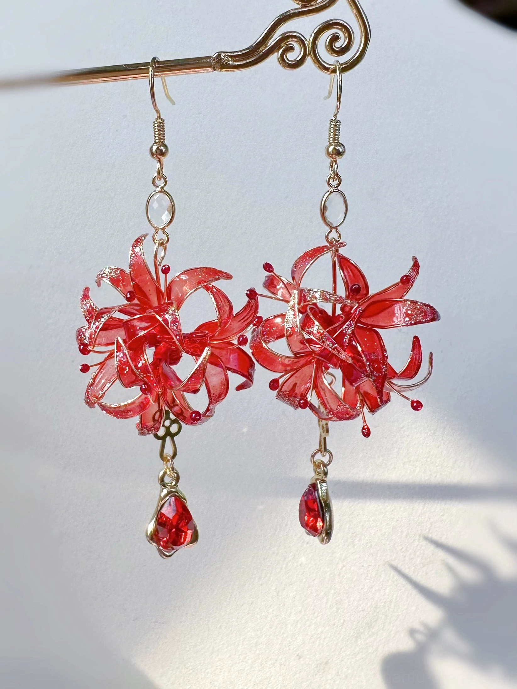 Red spider lily Hanfu earrings hanging from a vintage gold hairpin, showing red floral charms, crystal bead accents, gold ear wires, and teardrop red dangles