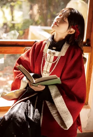 Red velvet Ming Dynasty modern hanfu cardigan outfit styled with a black inner blouse, cream trim, layered pearl necklaces, and red hair bow in a sunlit indoor setting