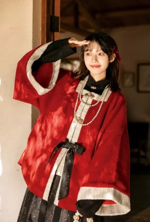 Front three-quarter view of a red velvet modern hanfu outer cardigan with black layered blouse, waist bow, gold details, and traditional Chinese styling
