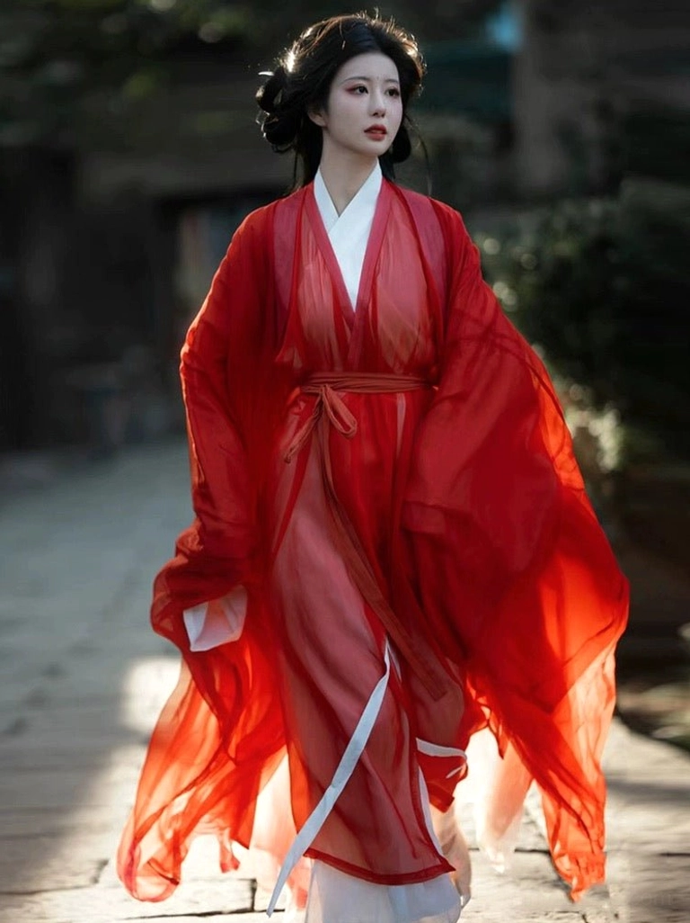 Front three-quarter view of a woman wearing a red Wei Jin Dynasty Hanfu robe with a sheer flowing outer layer, oversized sleeves, white inner robe, and red waist sash in an ancient Chinese stone alley