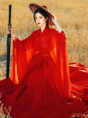 Red Wei Jin Dynasty qiyao ruqun Hanfu full set with flowing sheer sleeves and pleated floor-length skirt, modeled in a golden wheat field with a bamboo hat and sword