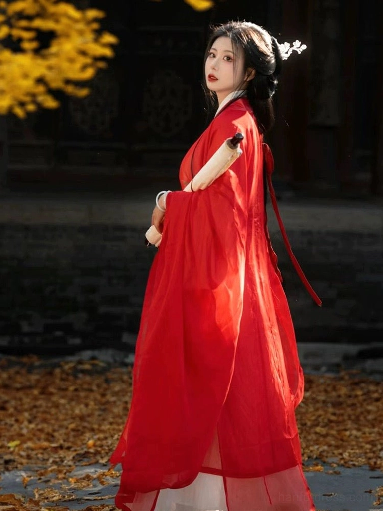 Side back view of a red Xianxia-inspired Wei Jin Dynasty Hanfu robe with trailing waist sash and sheer fabric, styled with a white floral hairpin and scroll among golden ginkgo leaves