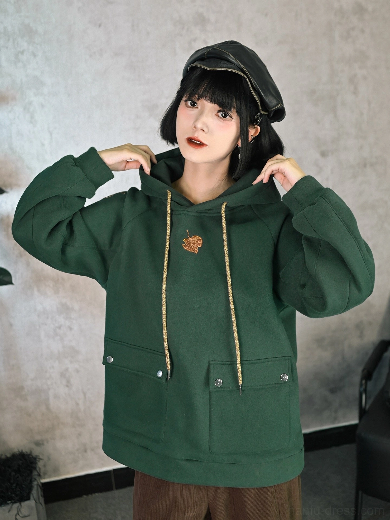 Close front view of dark green Modern Hanfu fleece hoodie with golden chest leaf embroidery, adjustable beige drawstrings, and snap button patch pockets