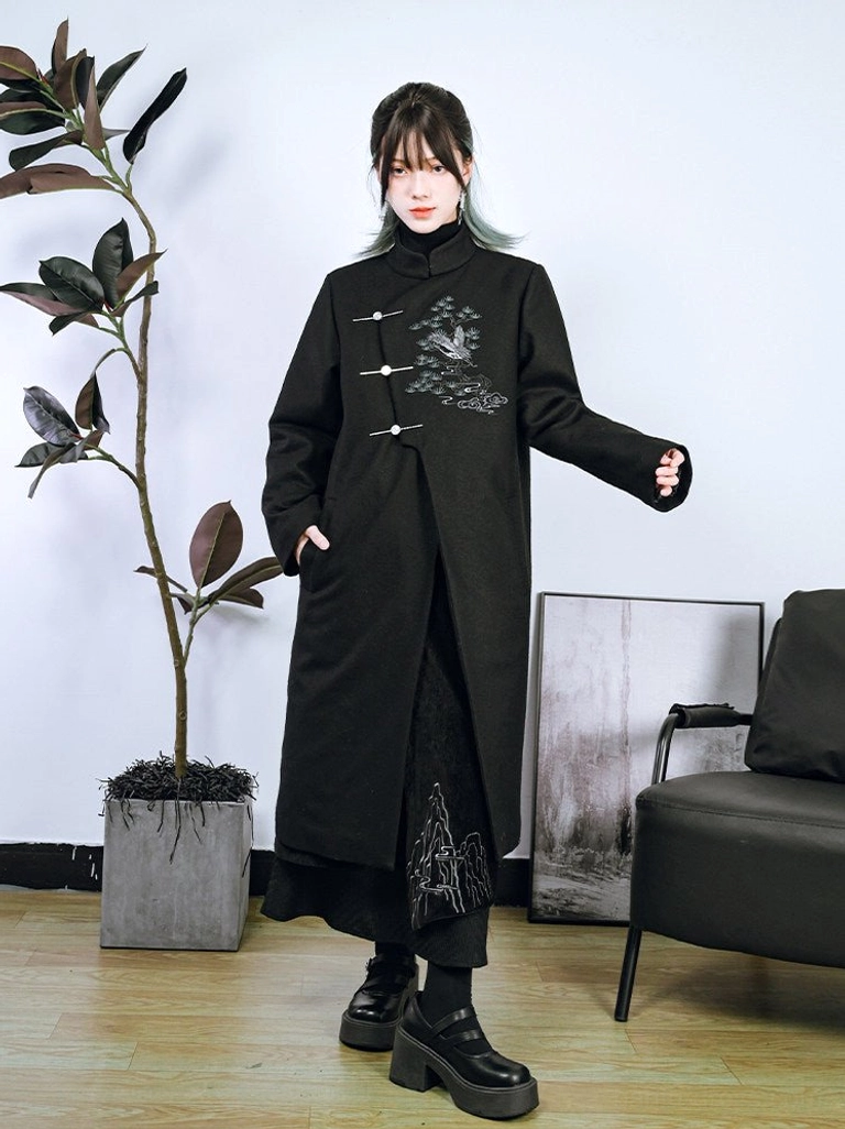 Side three-quarter view of a relaxed oversized Songhe embroidered modern Hanfu long coat styled with a black midi skirt and platform loafers