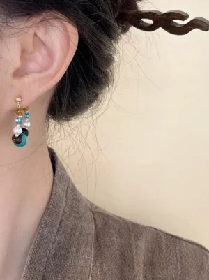 Retro Dunhuang Chinese hoop earrings with turquoise tiger eye beads faux pearls and crystal accents on an off-white background