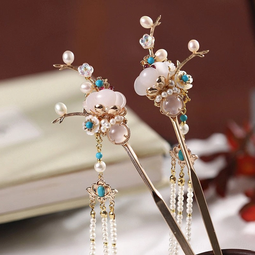 Oblique view of a matching pair of retro Chinese hair sticks with golden branches, milky white beads, turquoise-toned decorations, and long pearl tassels