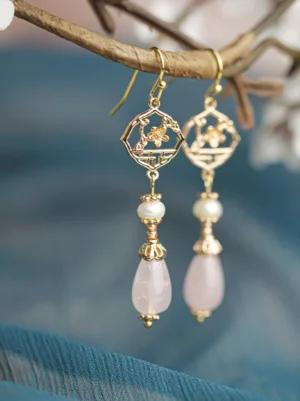 Retro pink pearl Chinese earrings with gold openwork window flower charms and pink teardrop pendants displayed on a dried flower branch