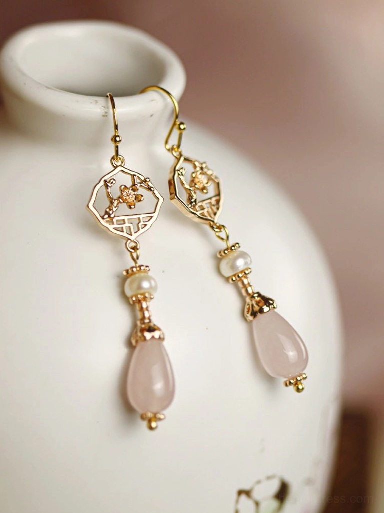Side close-up of retro Hanfu hook earrings with pearl beads gold floral window charms and pink teardrop pendants on ceramic vase