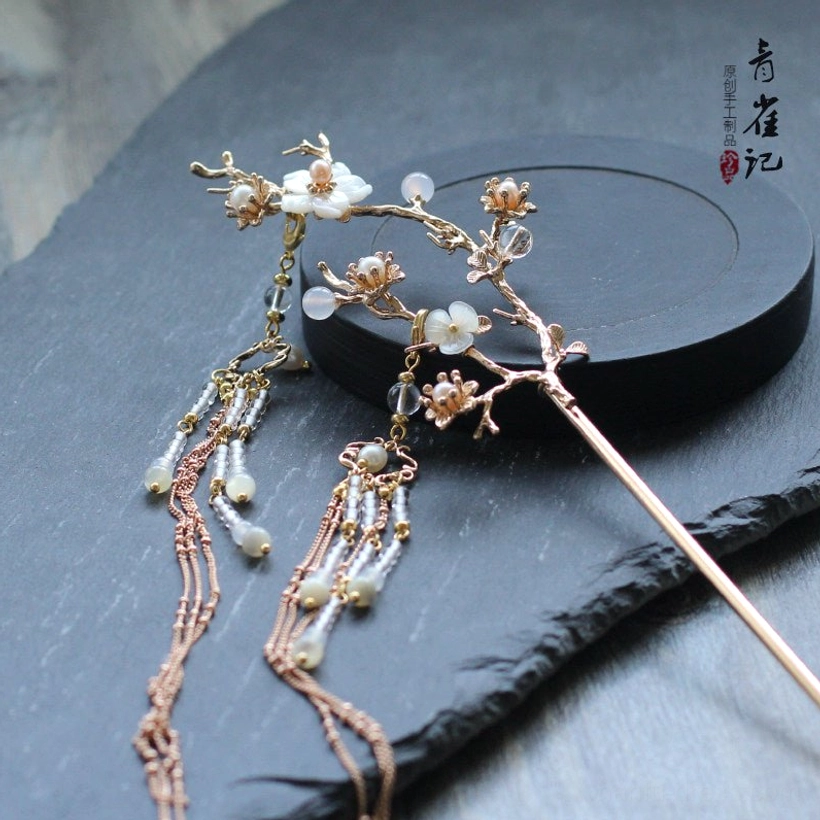 Full view of right pear blossom Chinese hair stick with white floral details, gold-tone branch, pearl-like beads, and long flowing tassel chains