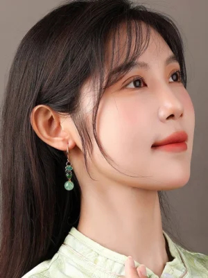 Model wearing Rising Clouds Chinese earrings with green bead pendants and traditional cloud motif beside a light green Hanfu-inspired top