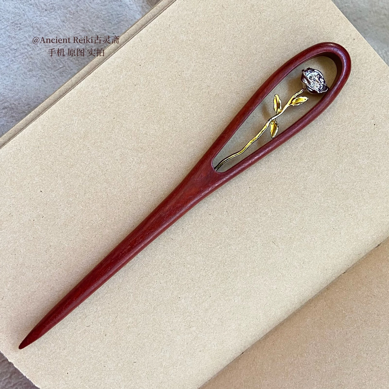 Traditional Chinese rose hair stick with reddish brown wooden hairpin and gold tone gem set rose ornament displayed on an open light colored notebook