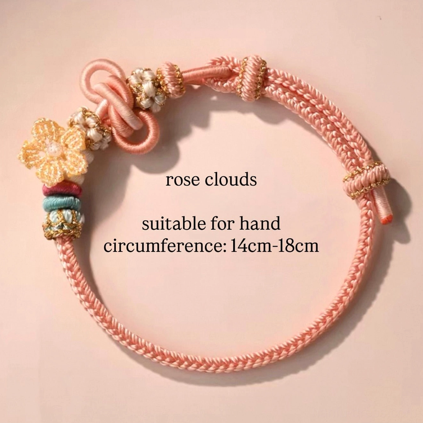 Rose Clouds handwoven Chinese knot bracelet in soft pink braided cord with floral charm, beads, and traditional knot accents on a light pink background