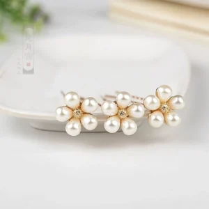 Set of three rose gold imitation pearl flower hair pins displayed on a white ceramic dish with soft green foliage