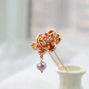 Rose gold peony Chinese hair stick with carved flower petals and dangling purple bead pendant displayed beside a white porcelain vase