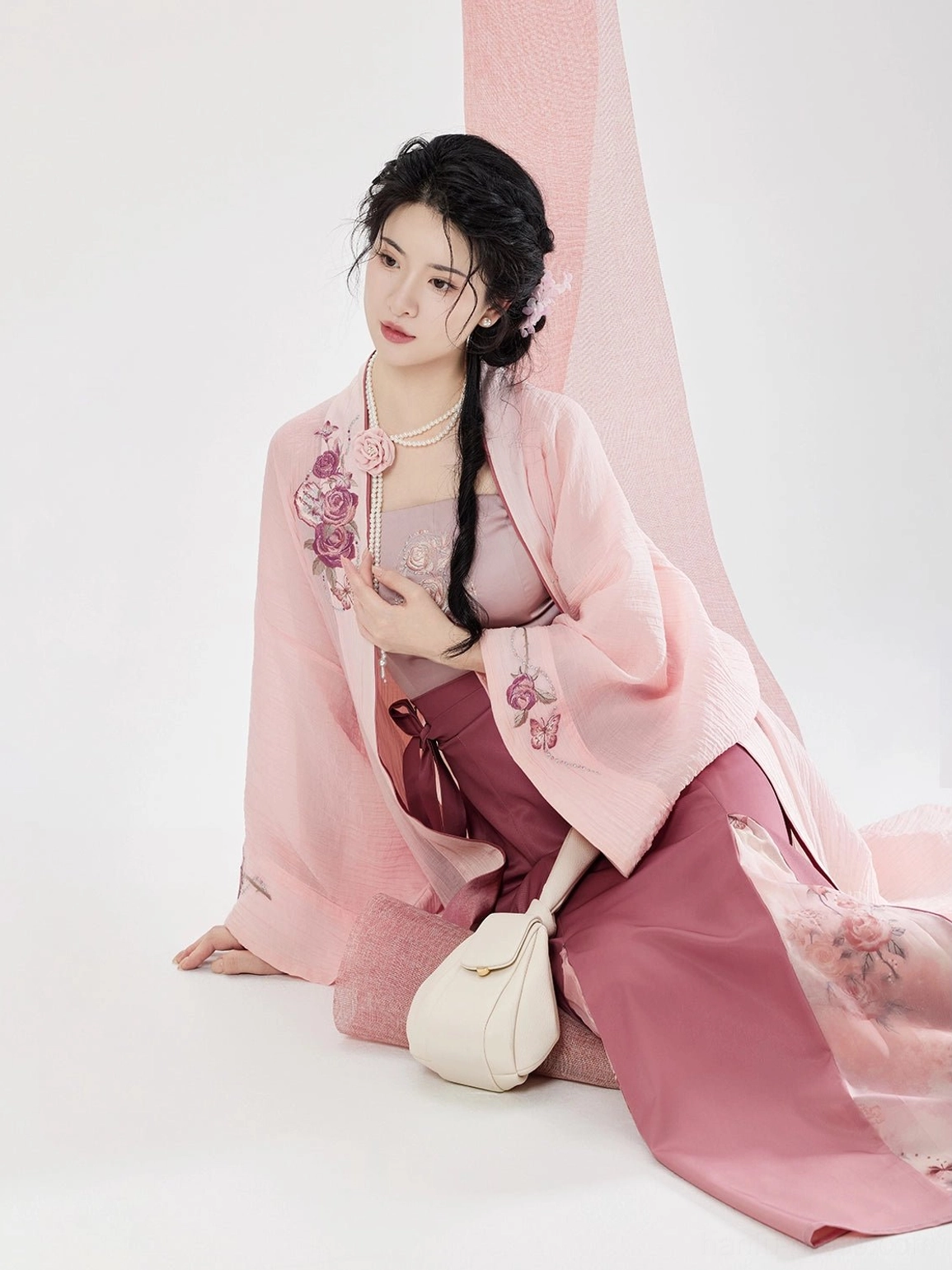 Rose pink Song Dynasty modern hanfu outfit displayed in a seated pose with flowing embroidered beizi jacket and lightweight layered skirt