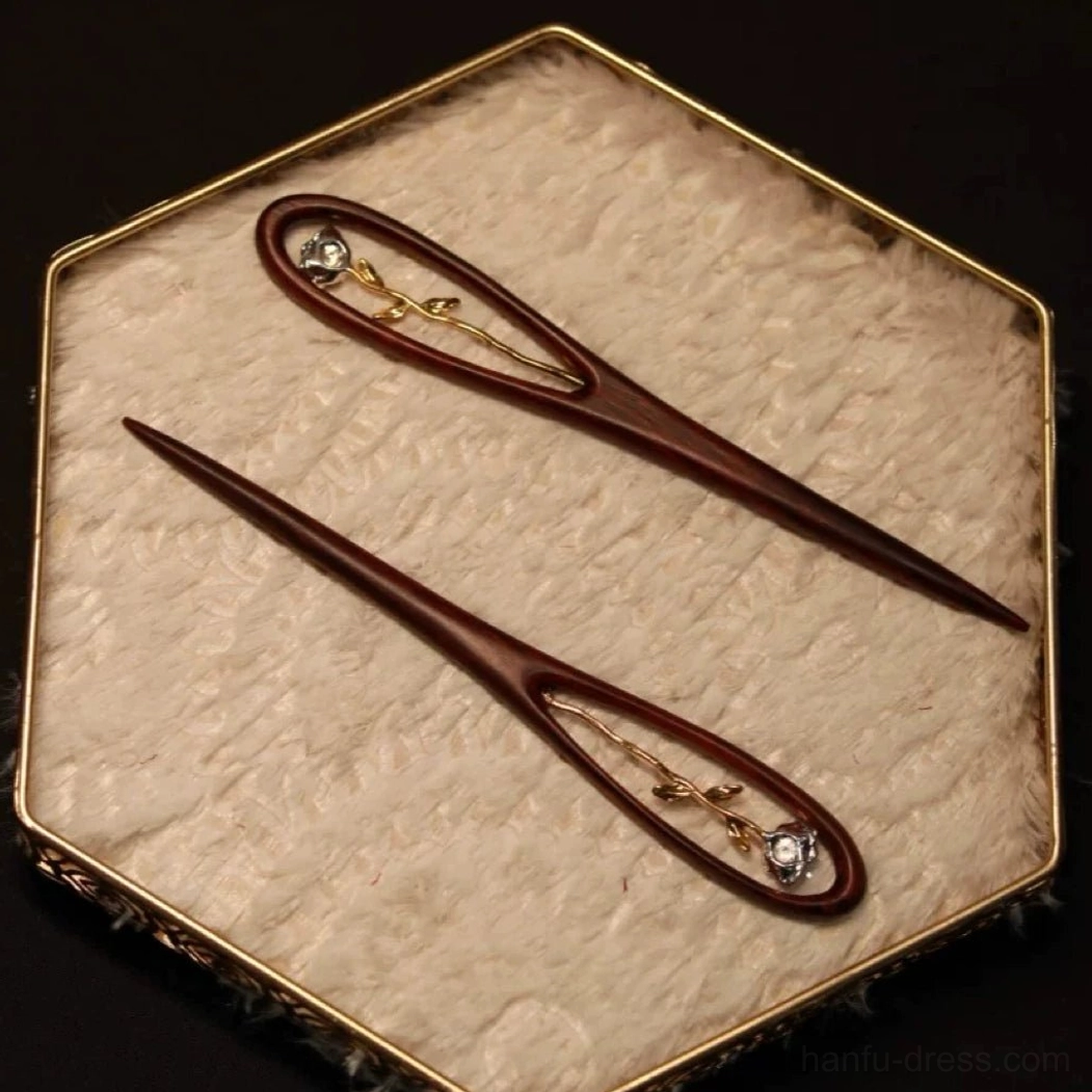 Two rose themed wooden Chinese hair sticks arranged in a gold framed velvet jewelry tray showing a decorated hairpin and a simple slender hair stick