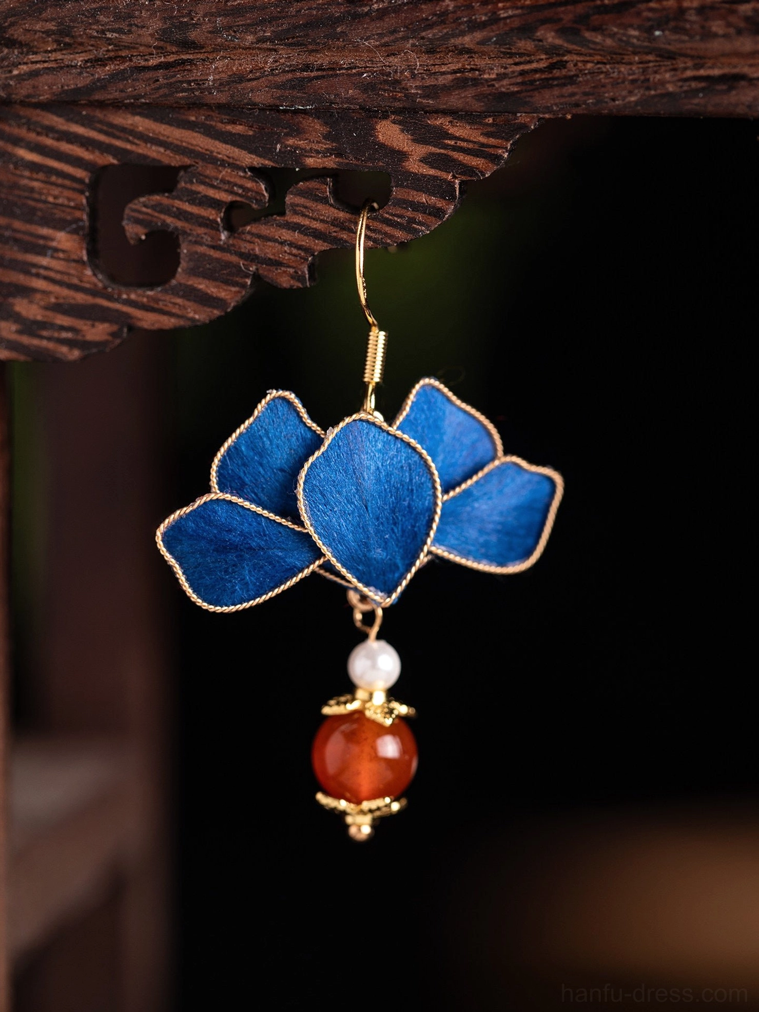 Single royal blue lotus Chinese hook earring hanging on carved wood stand with pearl and red agate-style drop