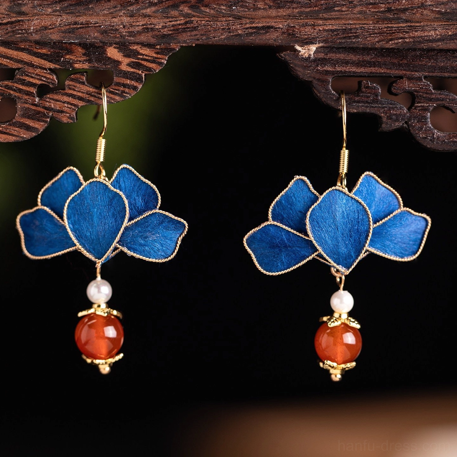 Pair of royal blue lotus hook earrings hanging on carved wooden jewelry stand with gold edging and red bead drops
