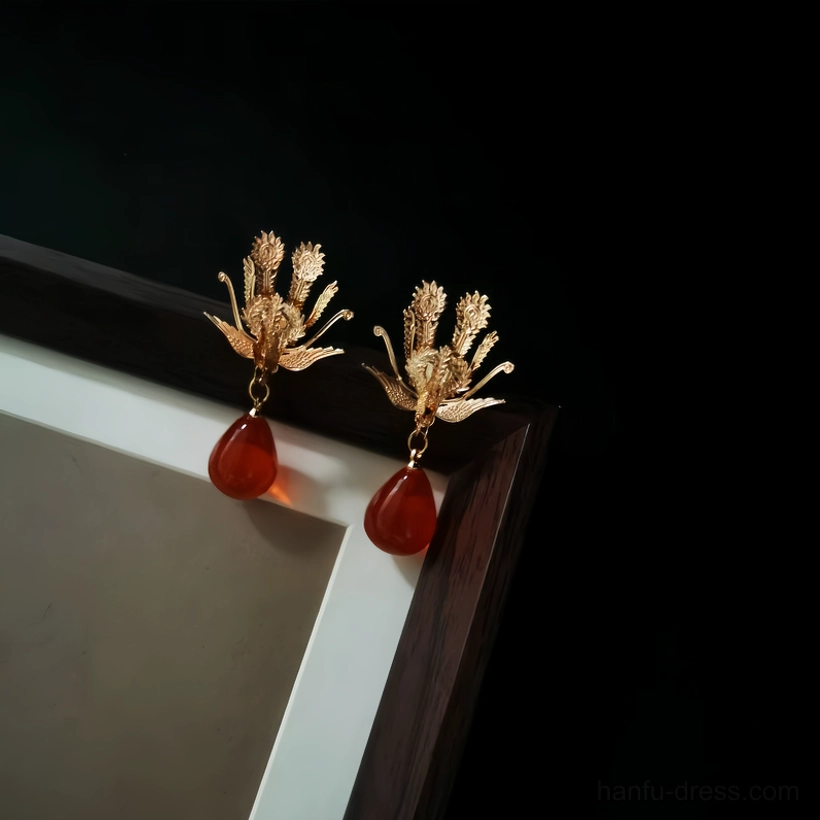 Gold ruby phoenix drop stud earrings displayed on a wooden frame against a black background, Chinese Hanfu jewelry pair with red teardrop pendants