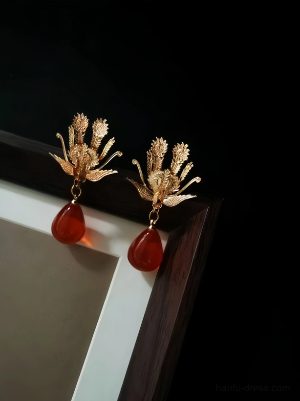 Front view of gold phoenix Chinese earrings with translucent ruby red teardrop pendants, elegant Hanfu jewelry on dark background
