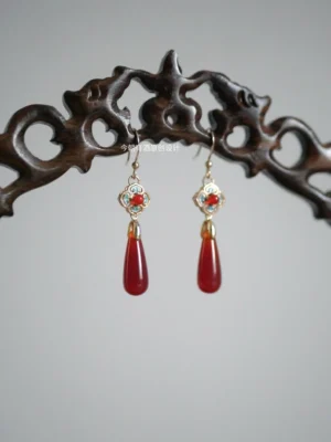 Ruby red agate flower drop earrings for Hanfu displayed on a carved dark wood holder with blue enamel accents and gold-tone setting