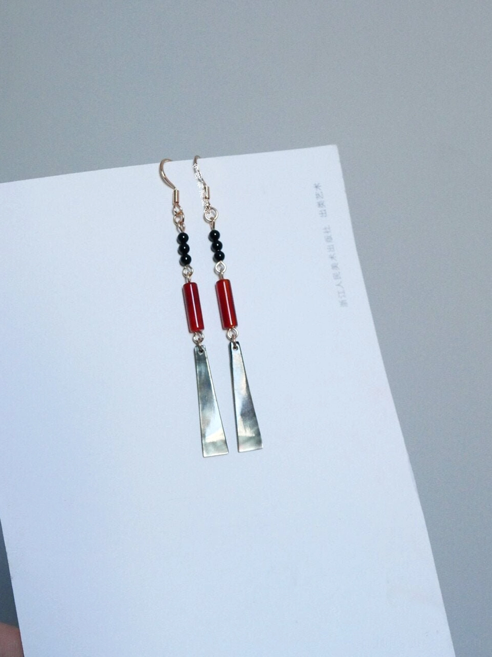 Black red and gold Chinese dangle earrings with trapezoid shell pendants shown in a front flat lay on a white book
