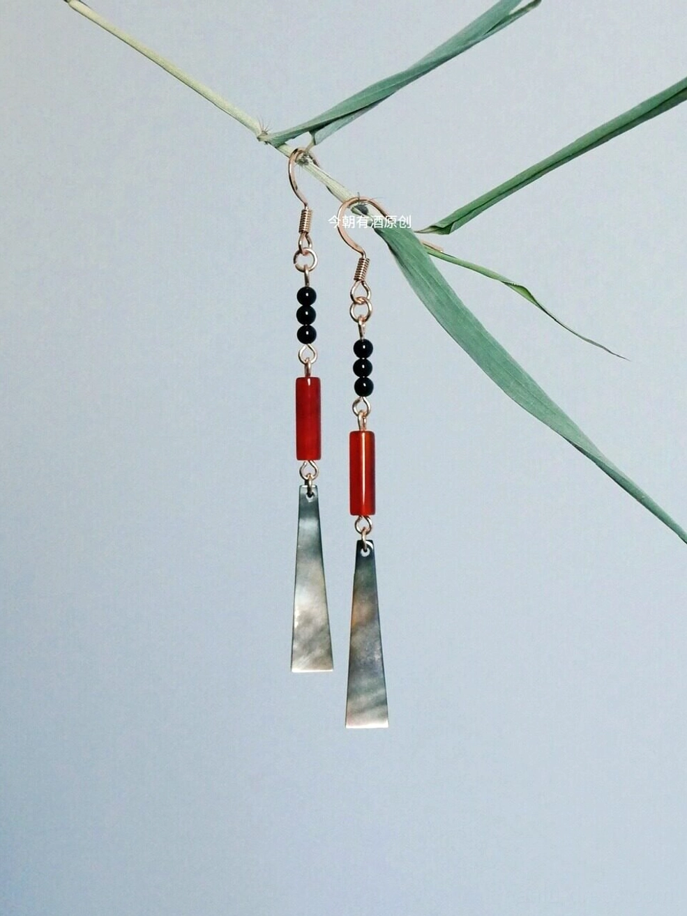 Ruby red shell drop Chinese earrings with black beads and gold hooks displayed beside green bamboo branches for Hanfu jewelry styling