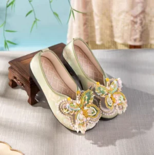 Sage green butterfly embroidered Chinese Hanfu shoes with beaded butterfly ornament and pearl tassels on traditional indoor display