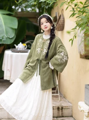 Chinese style sage green Hanfu winter jacket with wide bell sleeves, soft textured fabric, front tie closure, and white lace dress