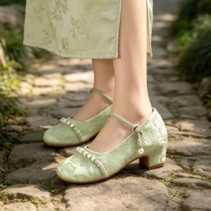 Woman wearing sage green floral jacquard Chinese Hanfu Mary Jane shoes with pearl ankle straps and low block heels while styling a traditional Cheongsam outdoors